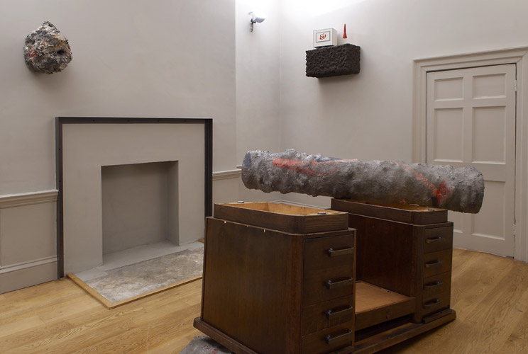 Phyllida Barlow and Steve Johnson 'Deep Time' 2009, from left to right: Phyllida Barlow, 'untitled: polystyrene, bonding plaster, cement, scrim, paint' 
            (40 h x 40 x 45 cm) 2009. Phyllida Barlow, 'Object for object series (ongoing since 1994) Object for an upturned desk 2009, cement over polystyrene, paint (130 h x 290 x 200 cm) Steve Johnson, 'Acht Uhr Dreiig' 2009, mixed media (65 x 65 x 35 cm) go to Sharon Kivland's page